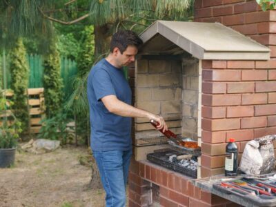 A man grills meat on a brick barbecue in the garden, showcasing outdoor cooking and leisure activity.