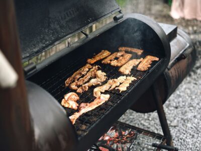 Close-up of a barbecue grill outdoors with various meat strips cooking, exuding rich smoke.