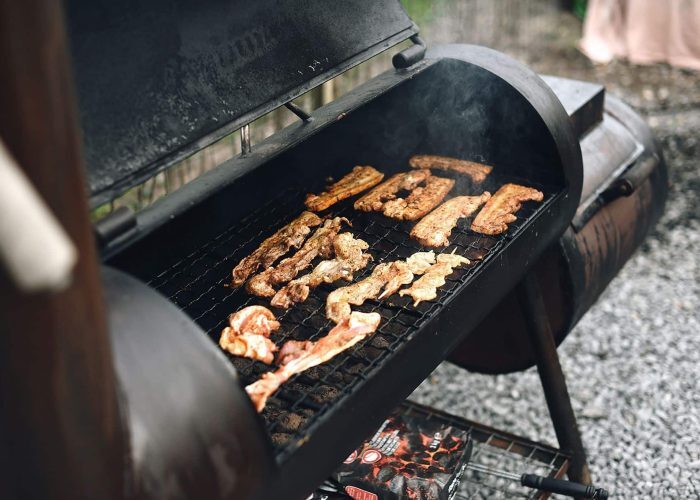 Close-up of a barbecue grill outdoors with various meat strips cooking, exuding rich smoke.