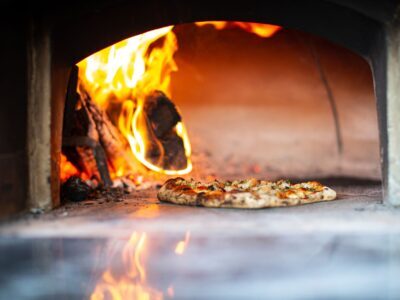 Delicious artisan pizza baking in a traditional wood-fired oven with flames.