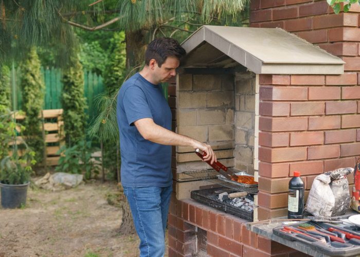 A man grills meat on a brick barbecue in the garden, showcasing outdoor cooking and leisure activity.