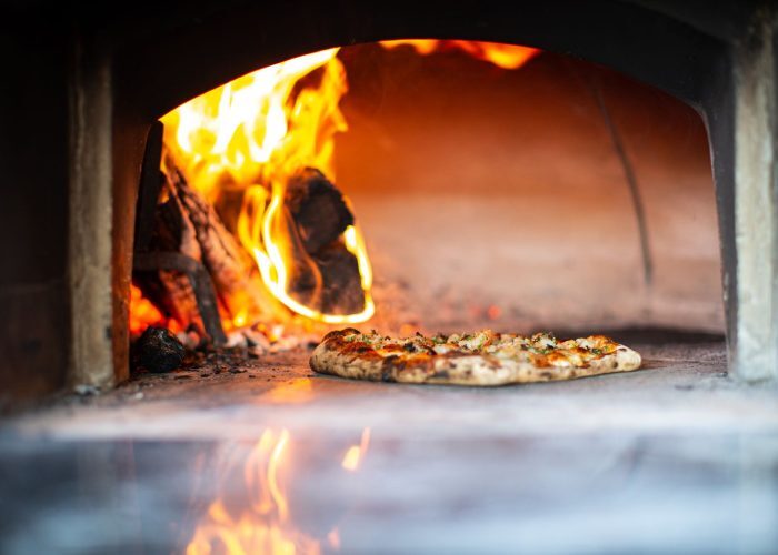 Delicious artisan pizza baking in a traditional wood-fired oven with flames.